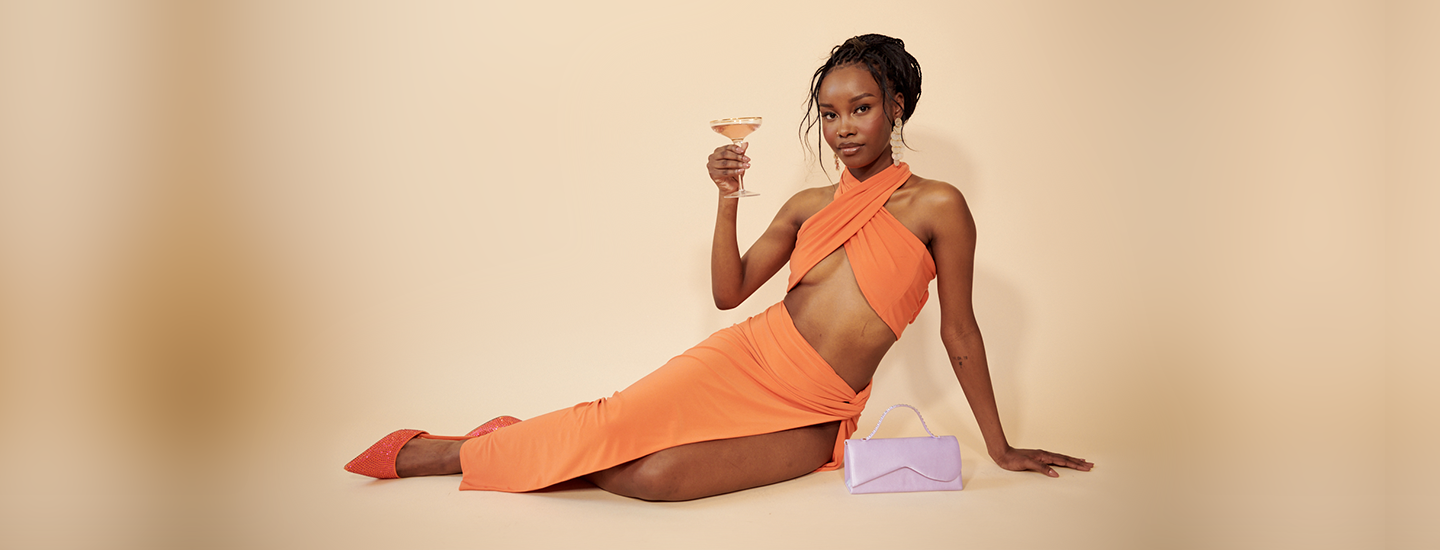 woman in an orange formal dress lying on her side holding a drink, orange dress, fashion, style, black-owned fashion brands, black-owned brands, fashion brands, brutal fruit, the suite, the suite edit